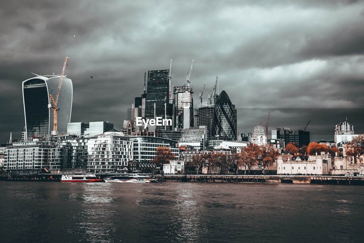 Modern buildings by river against sky in city