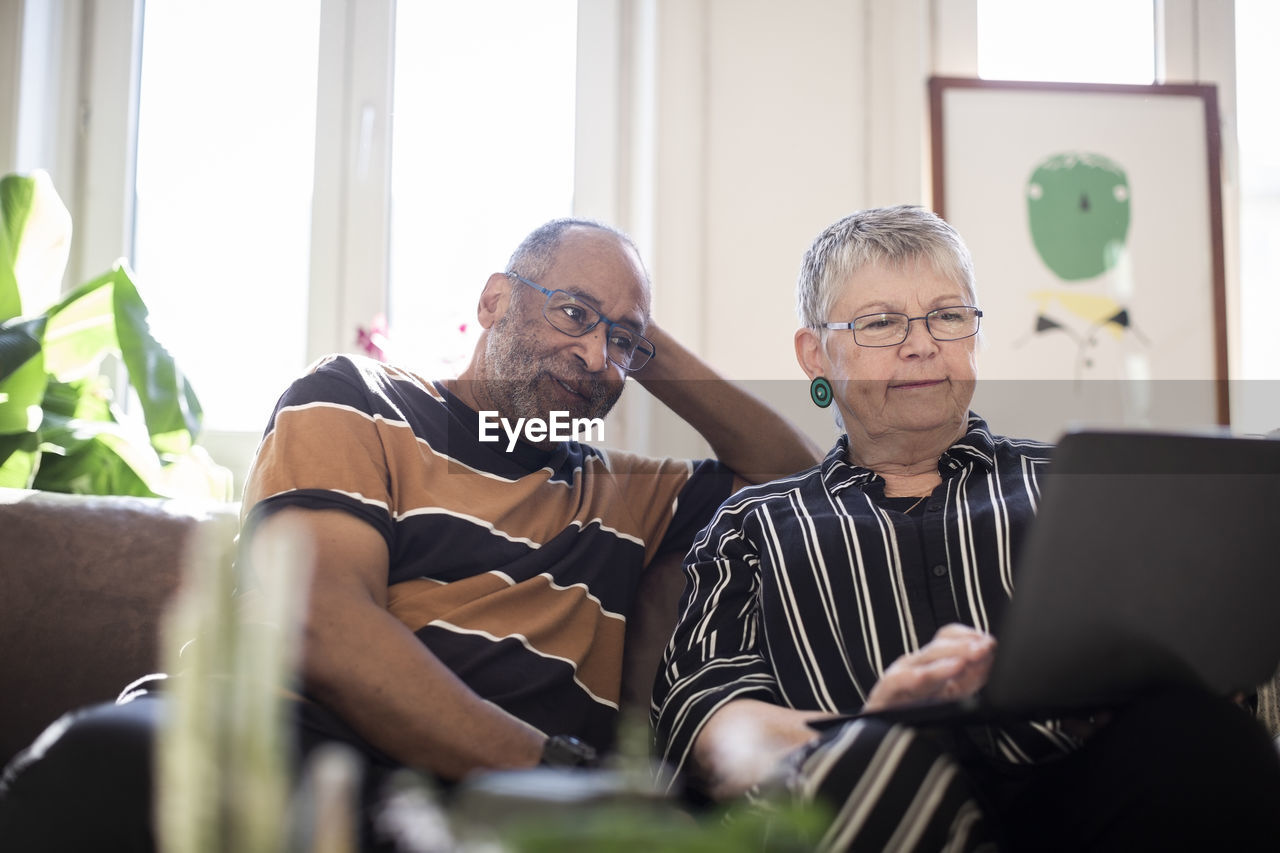 Woman using laptop while man sitting by on sofa