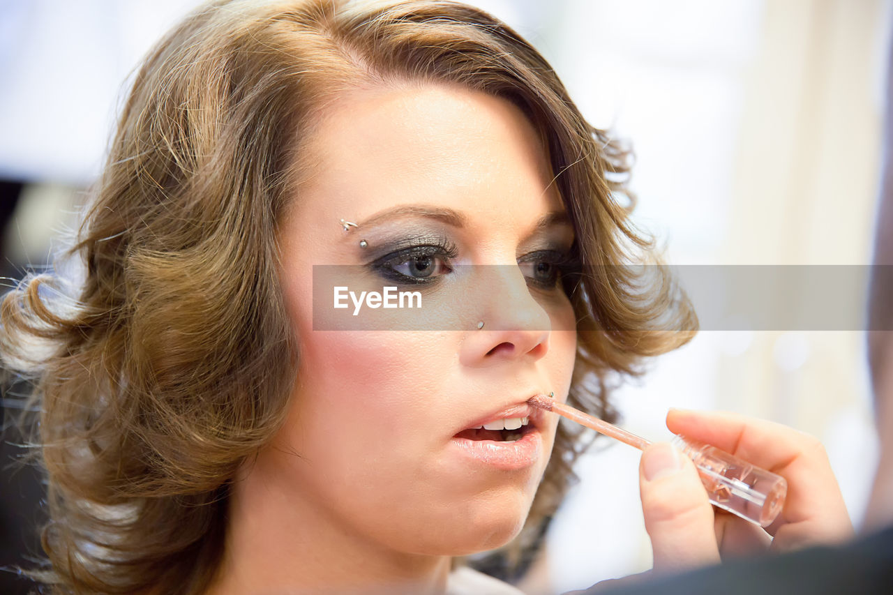 Close-up of woman with short hair applying lip gloss