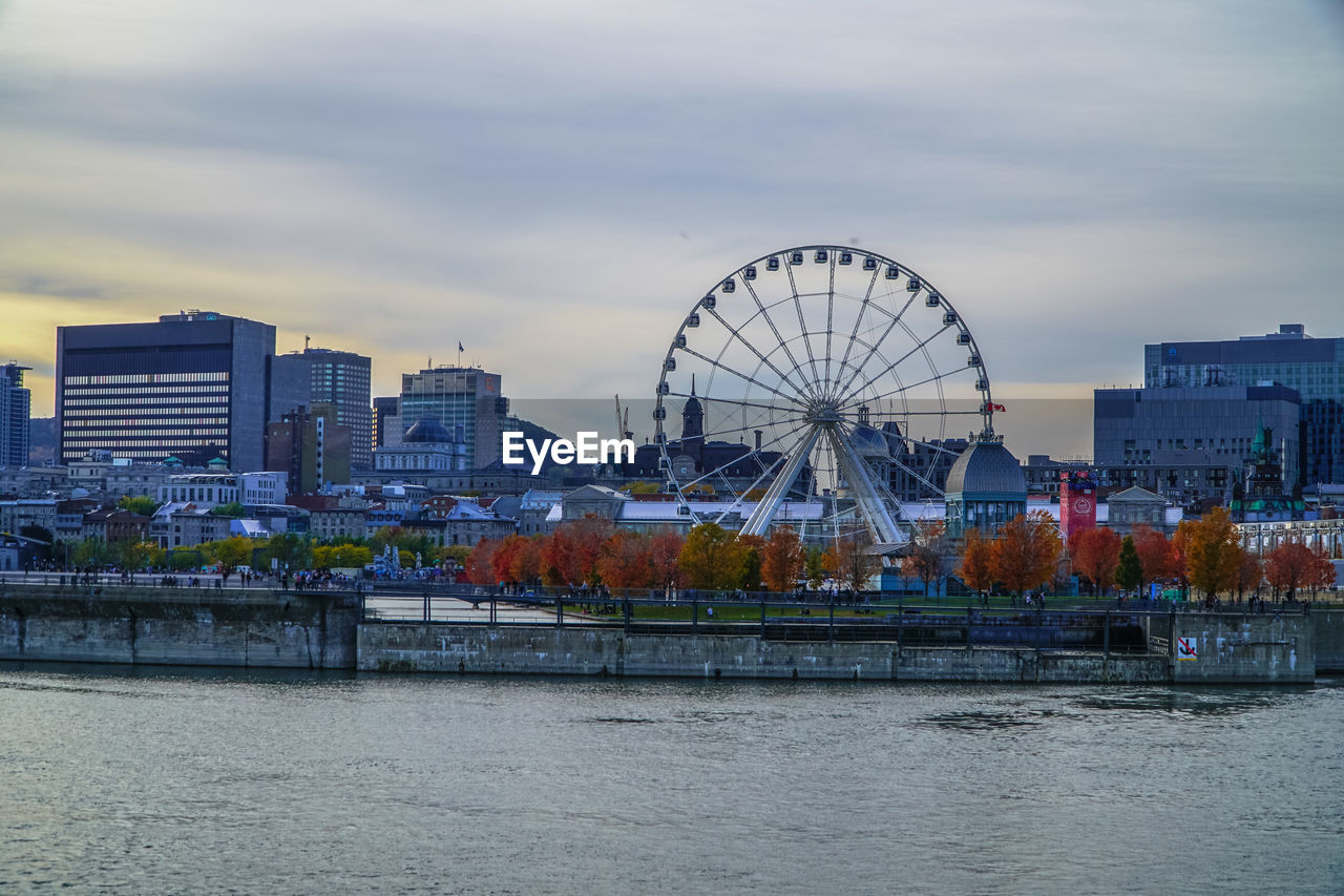 Ferris wheel by river in city against sky