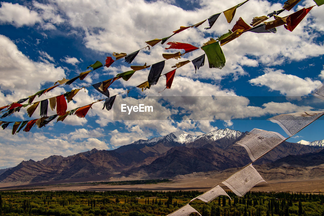 LOW ANGLE VIEW OF FLAGS HANGING AGAINST MOUNTAINS