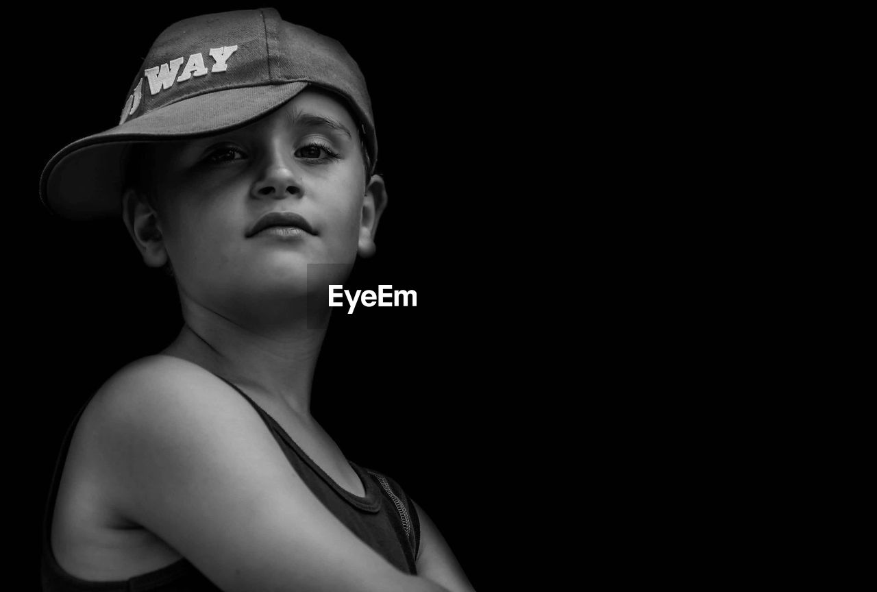 Portrait of boy wearing cap while standing against black background