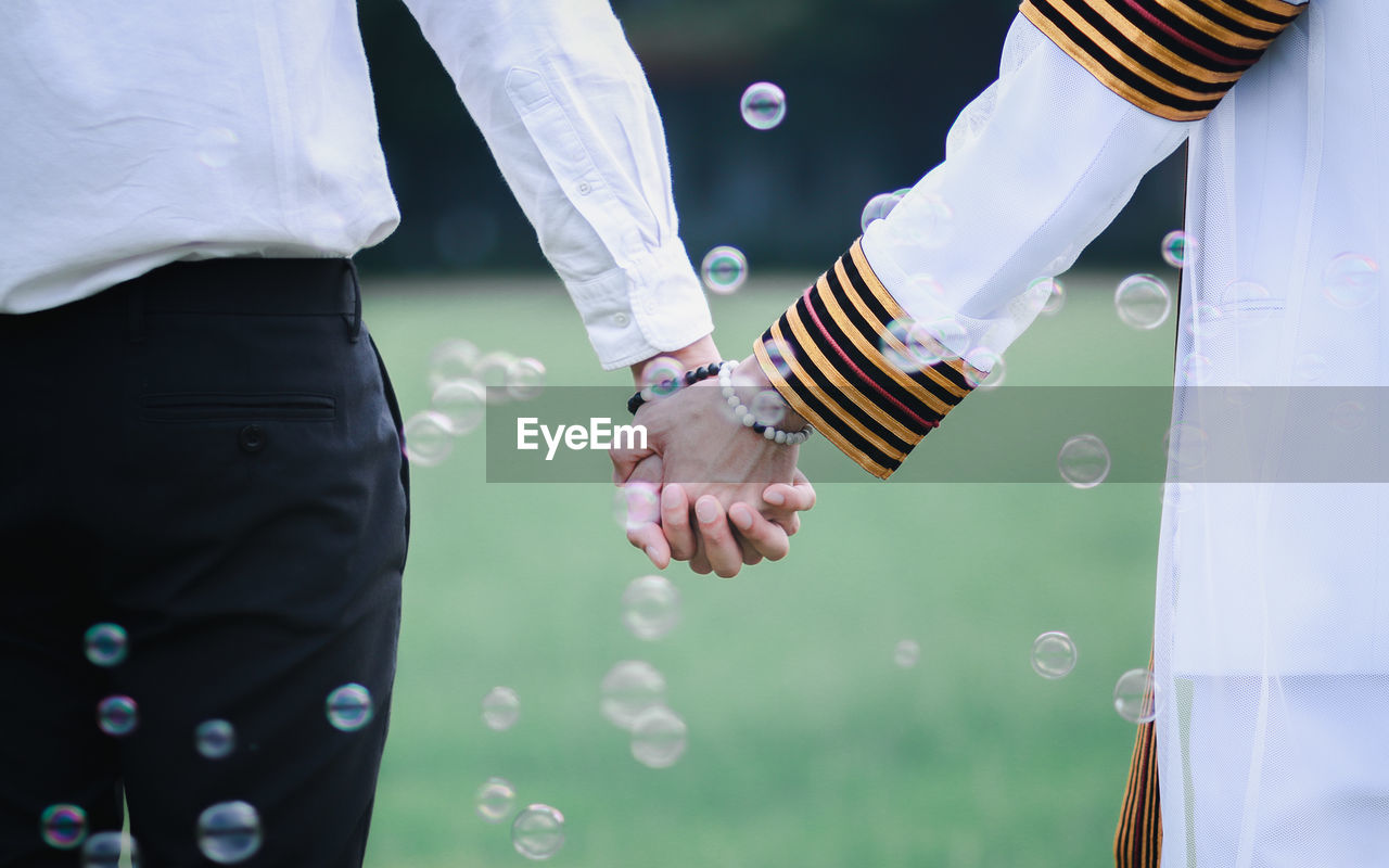 Midsection of couple holding hands amidst bubbles