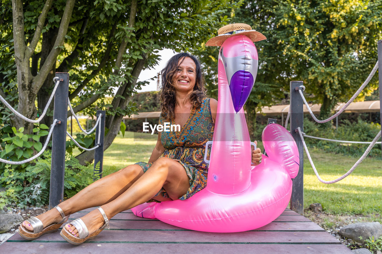 Portrait of beautiful middle aged woman sitting on pink flamingo inflatable toy