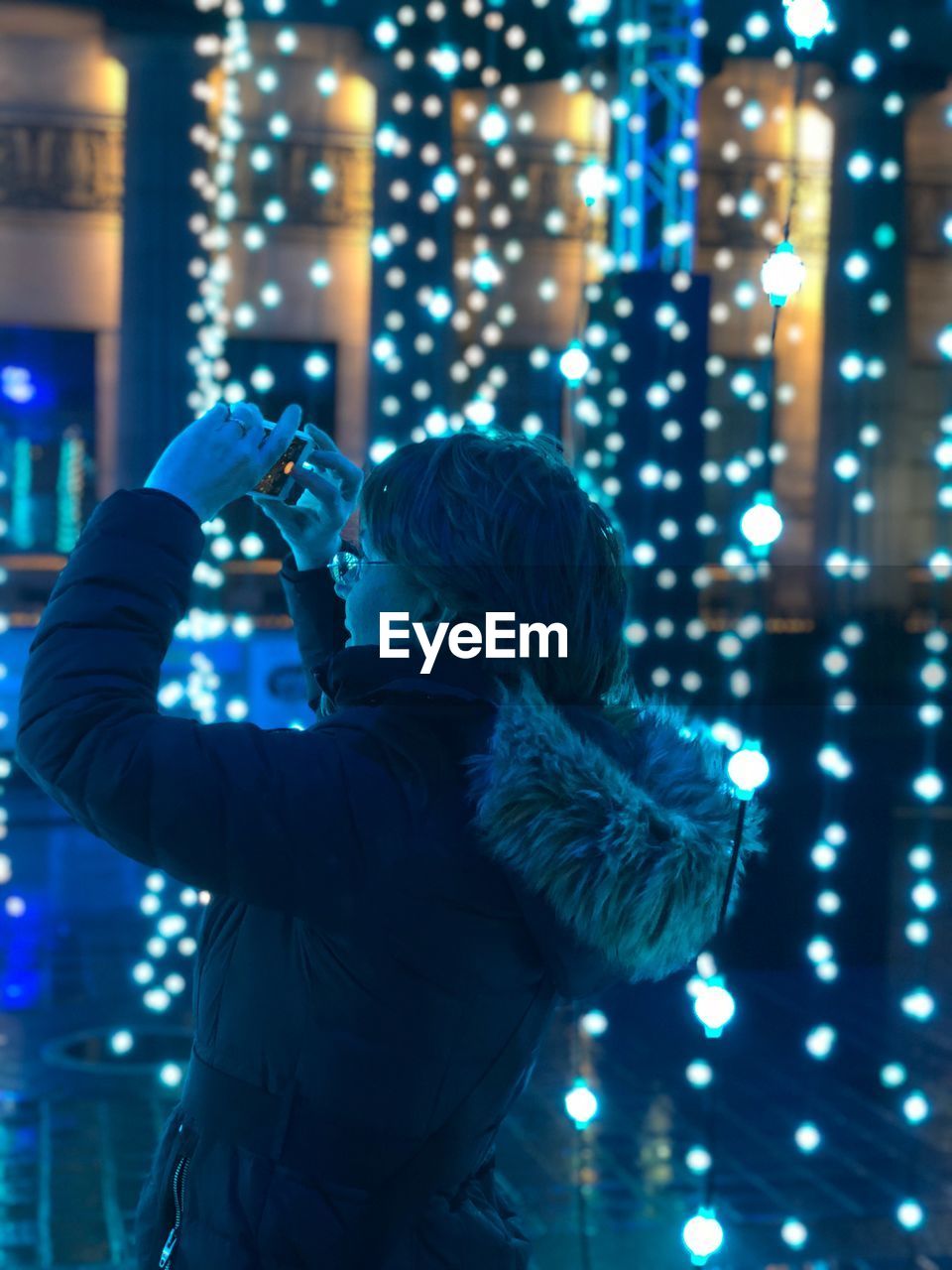 Side view of woman photographing by lights at night