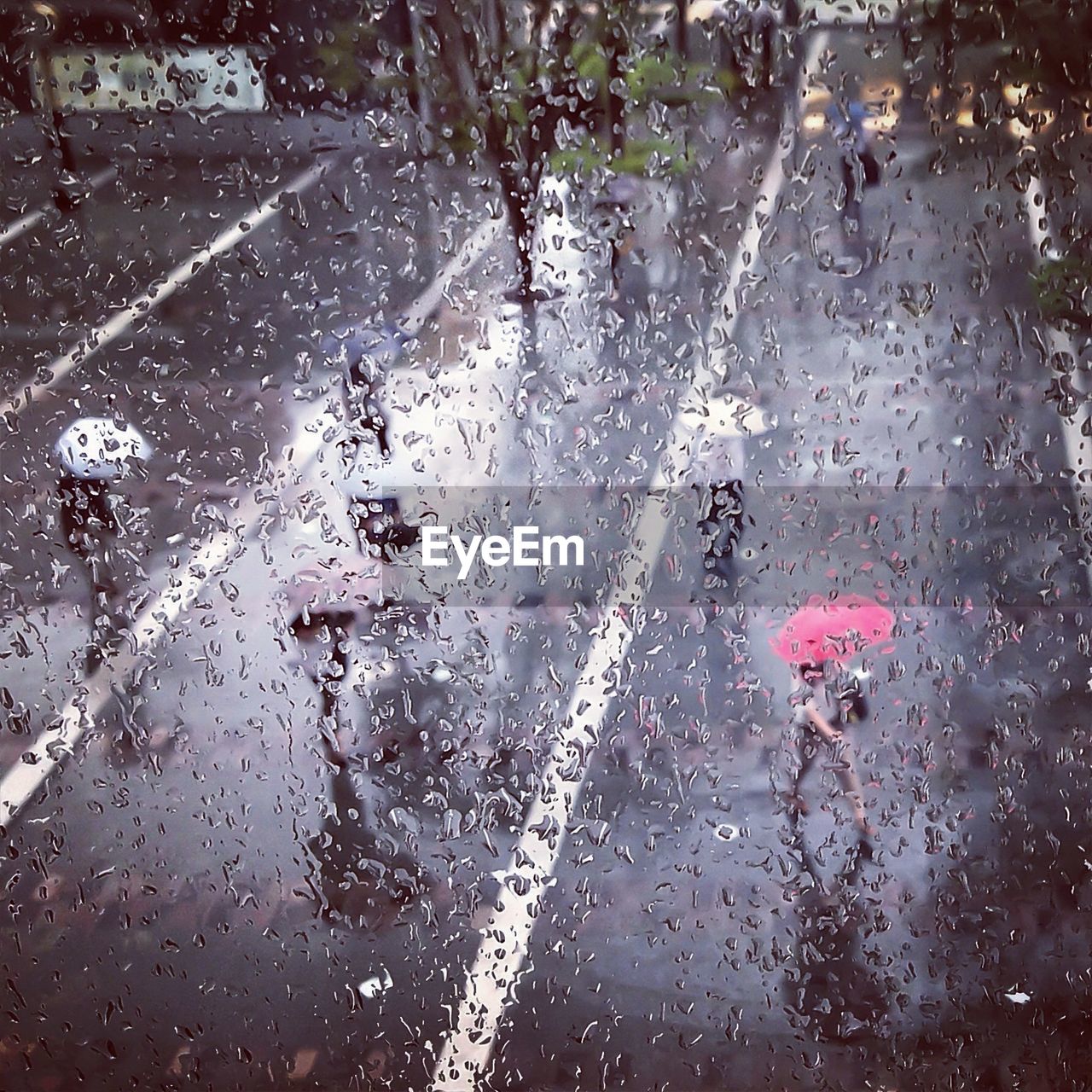 Waterdrops on glass against people walking with umbrellas on road