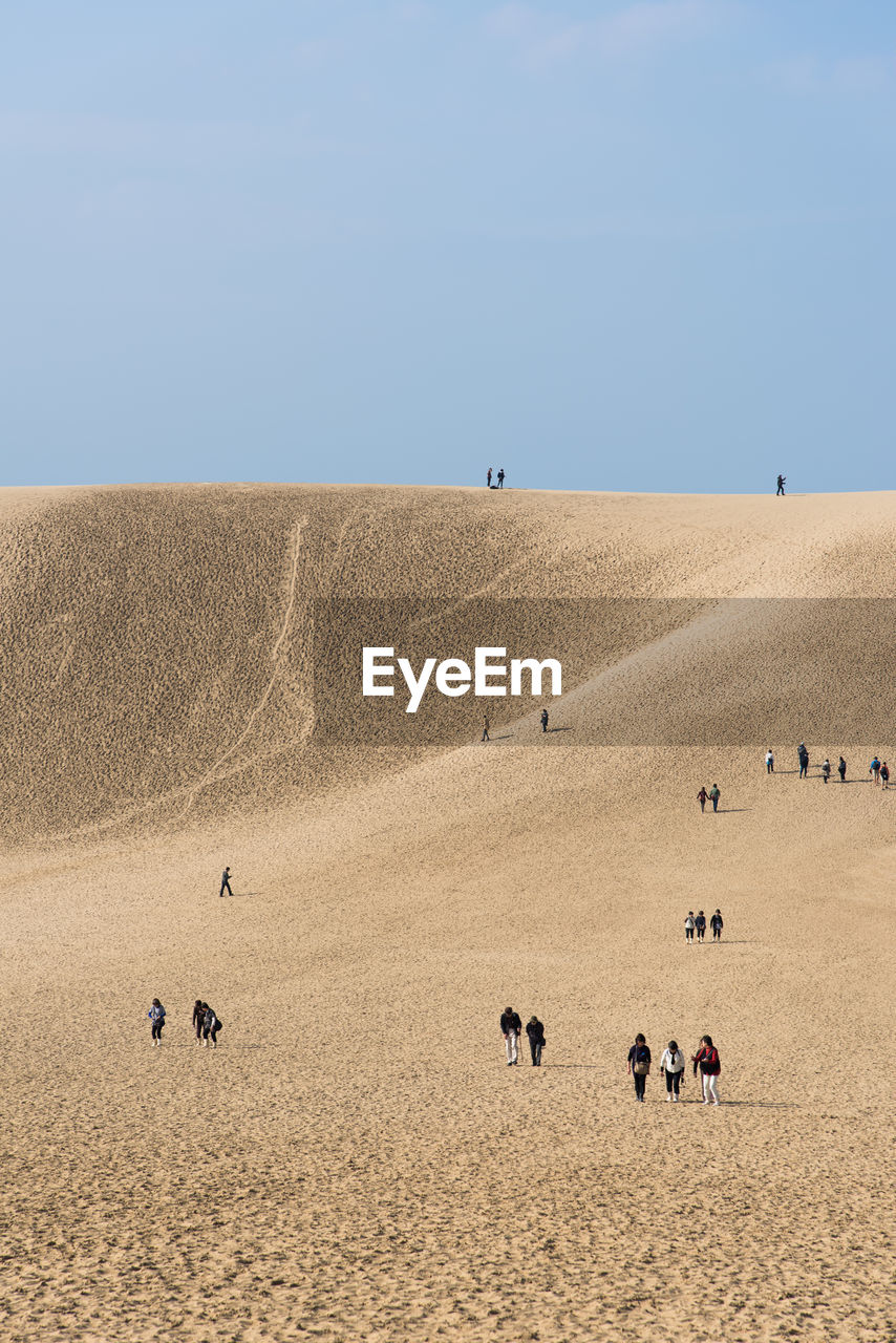 People on sand dune against clear sky