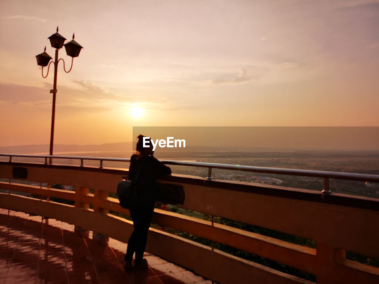 Woman standing by railing against sky during sunset