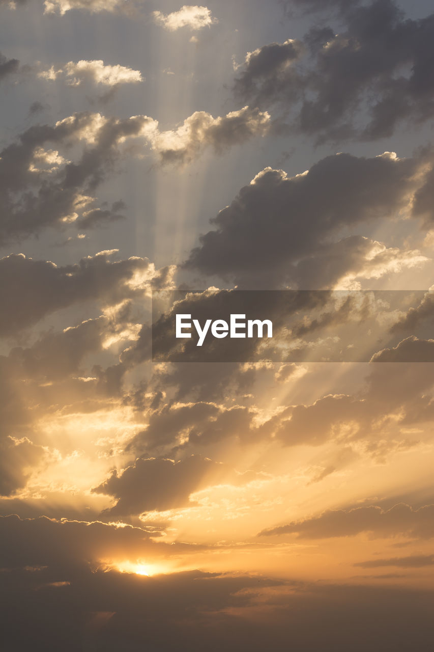 Sunrise with dramatic dark clouds and light rays through clouds at sky, vertical shot