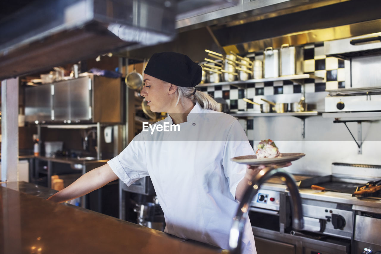 Female chef holding plate in kitchen at restaurant