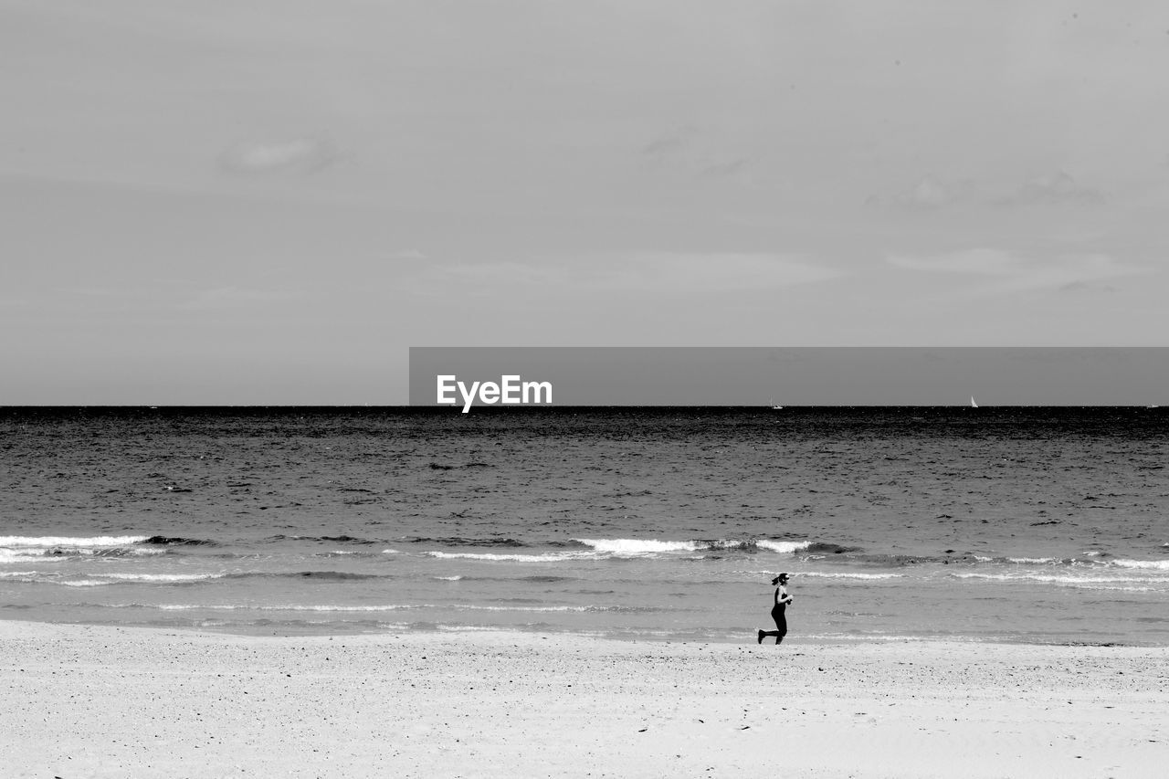 MAN STANDING ON BEACH BY SEA AGAINST SKY