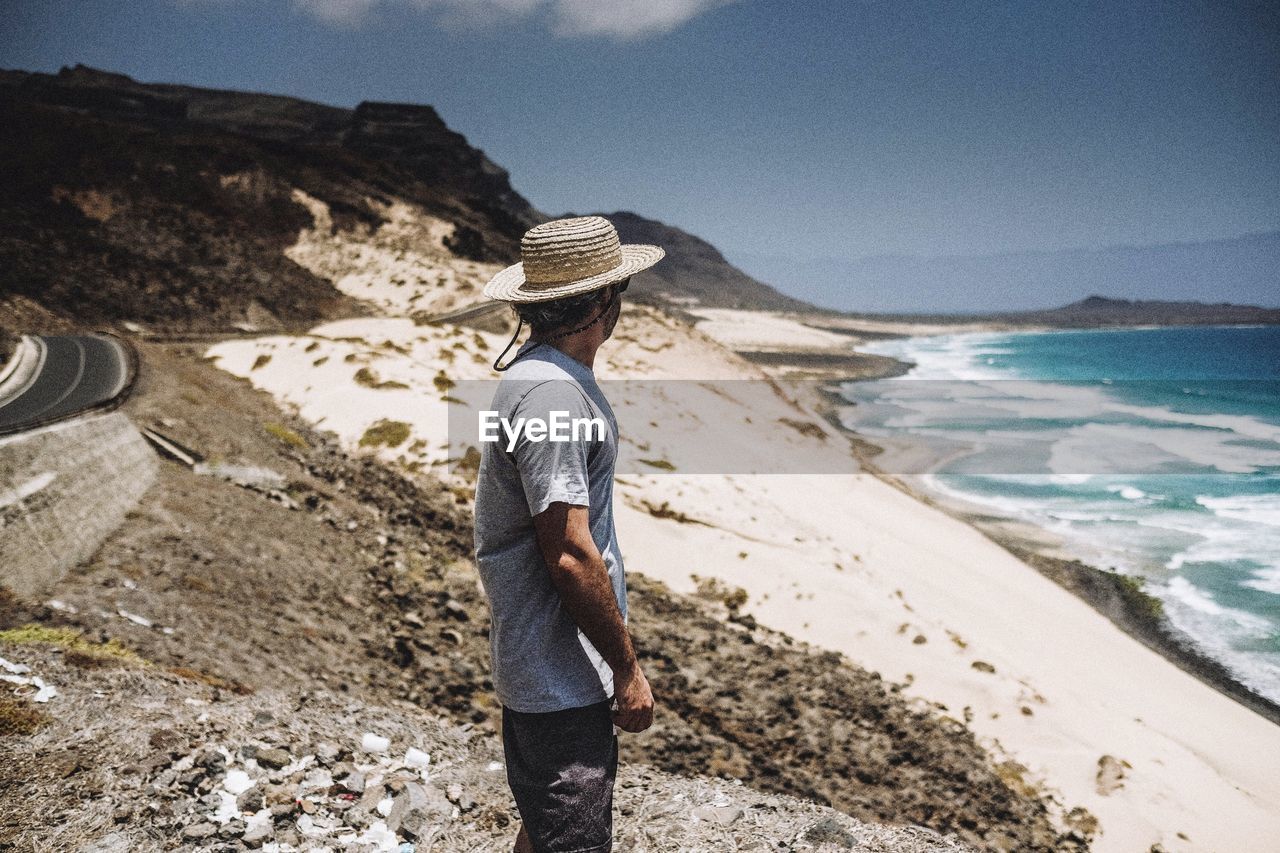 Side view of man standing at beach during sunny day