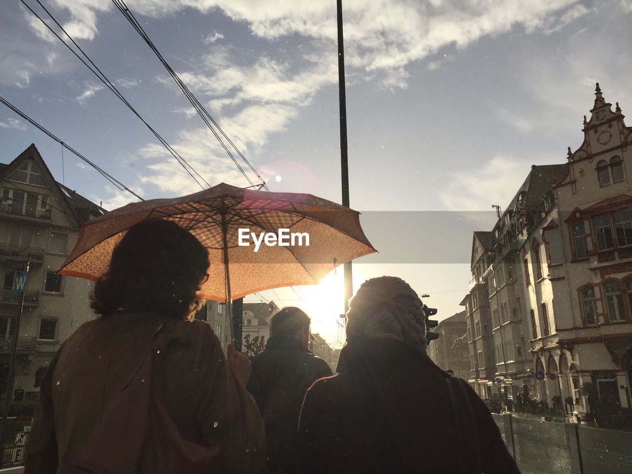 PEOPLE WALKING ON CITY STREET AGAINST CLOUDY SKY