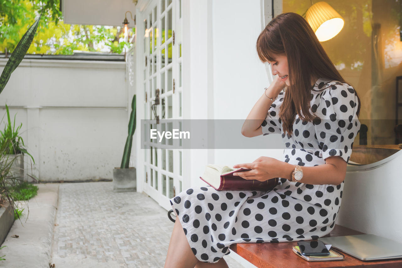 YOUNG WOMAN USING MOBILE PHONE WHILE STANDING ON LAPTOP AT HOME