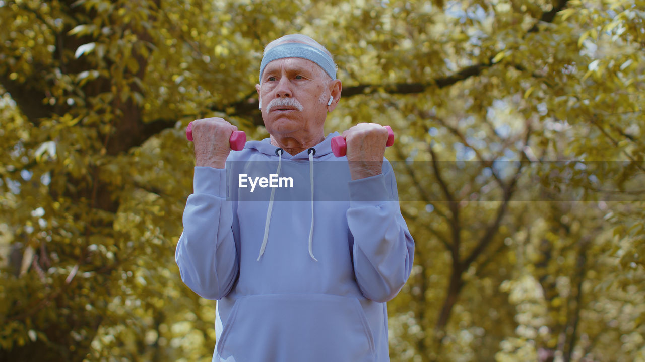 Dedicated senior man exercising with dumbbells in park