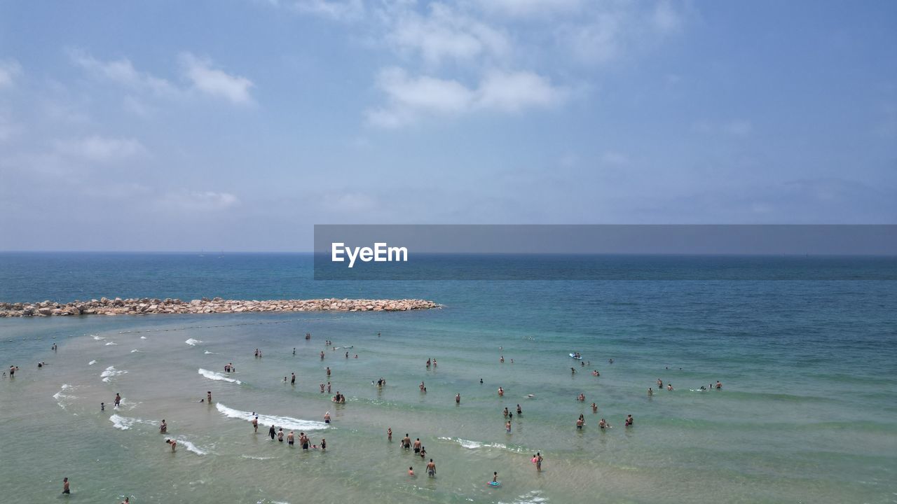 sea, water, sky, land, beach, horizon over water, horizon, body of water, large group of people, scenics - nature, crowd, shore, ocean, nature, group of people, beauty in nature, cloud, vacation, coast, holiday, trip, travel, sand, travel destinations, tourism, day, leisure activity, tourist, bay, outdoors, tranquility, coastline, sports, tranquil scene, blue, idyllic, summer, non-urban scene, high angle view, lifestyles, swimming
