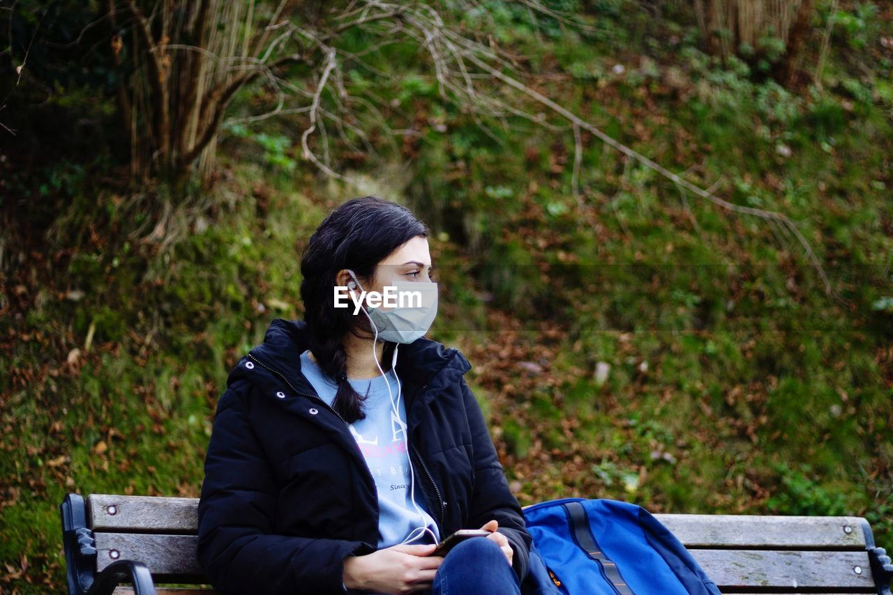 Young woman wearing mask sitting on bench