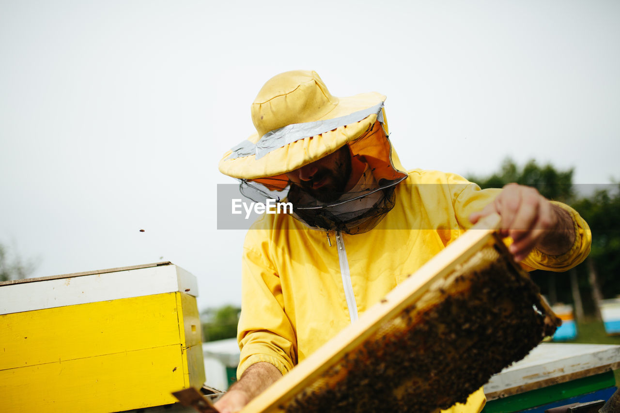 Low section of man holding yellow umbrella against clear sky