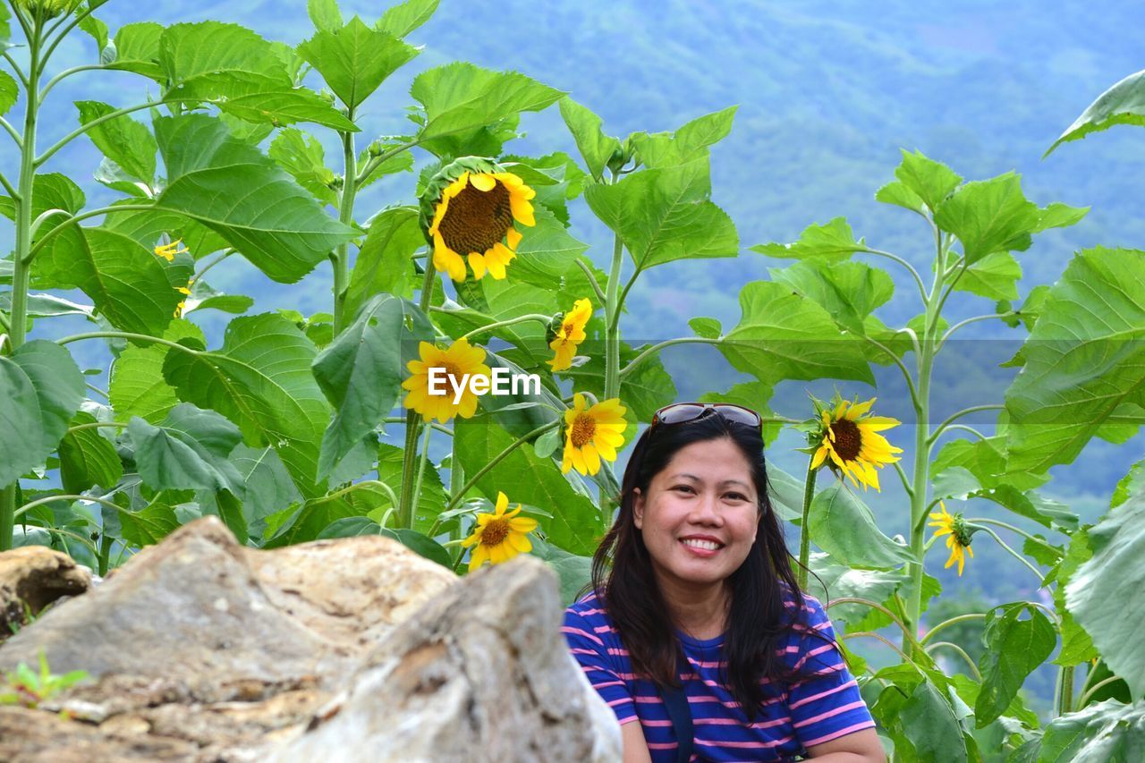 Portrait of smiling woman by sunflowers plant against mountain