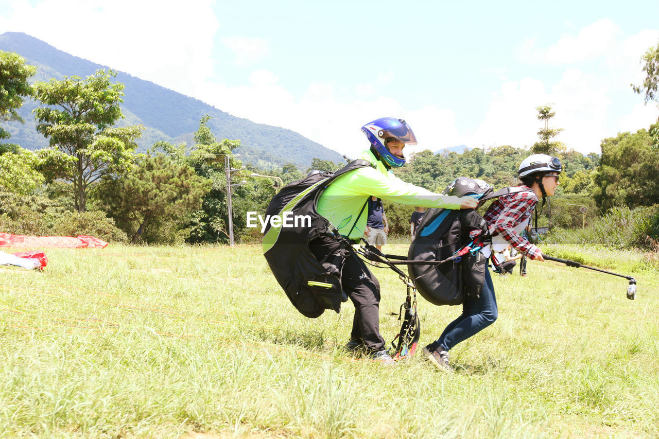 Couple paragliding on grassy field against clear sky