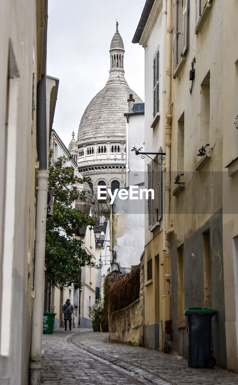 View of famous church sacre coeur in paris through narrow side alley laid with cobblestones. 