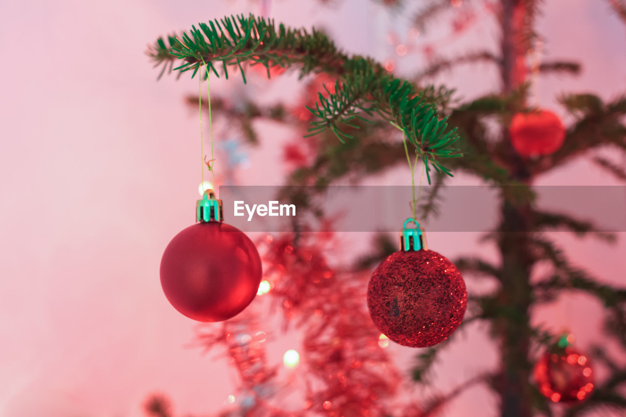 Two round red baubles hanging on a christmas tree with red lights.