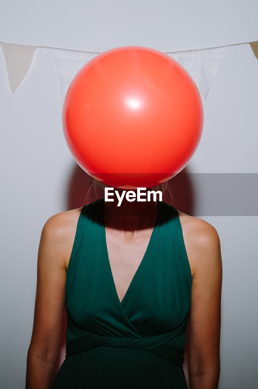 Midsection of a woman with red balloon against wall