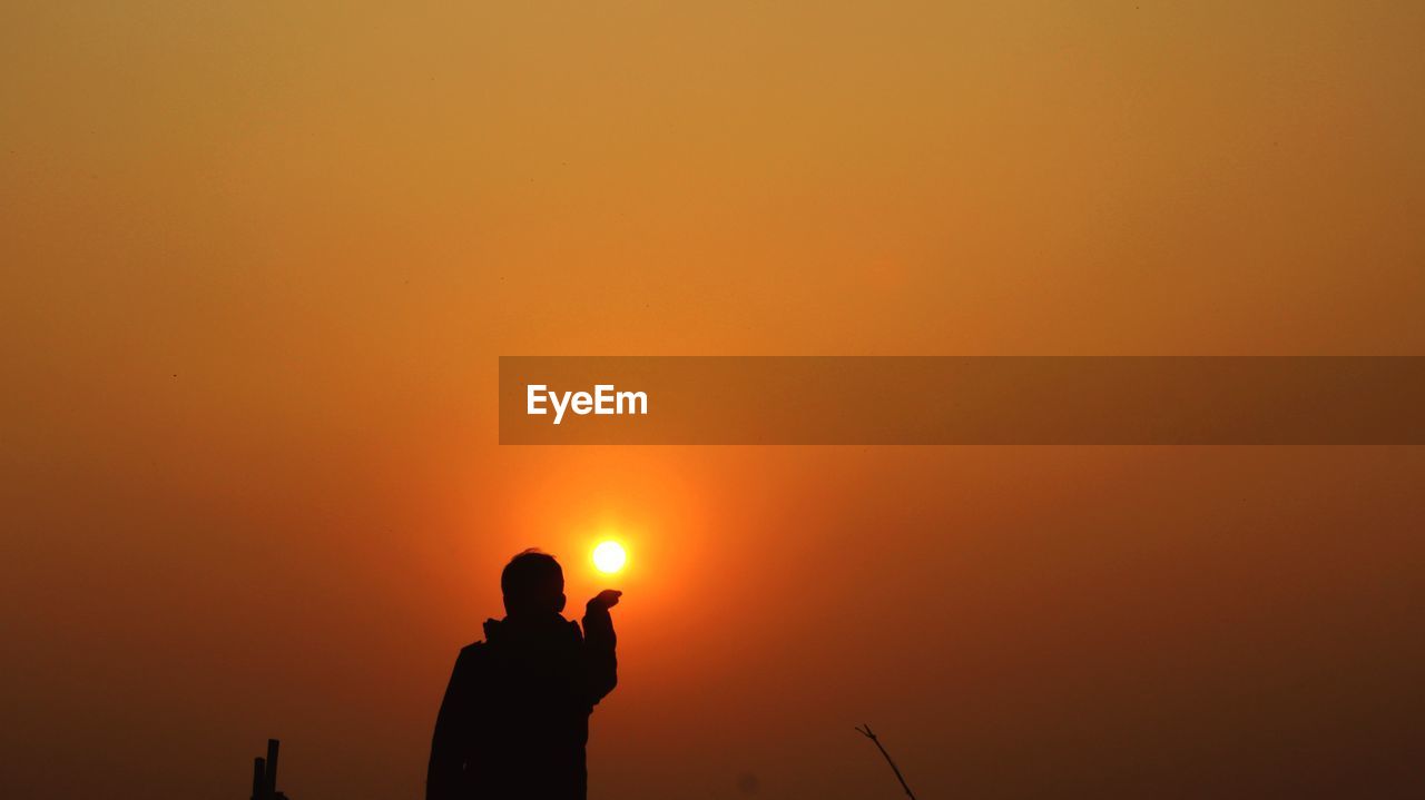 Silhouette man photographing orange sky during sunset