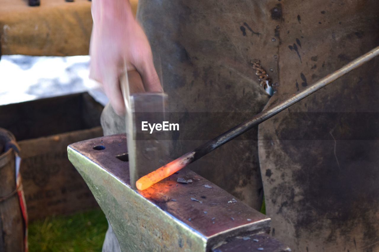 Midsection of worker working on metal at factory