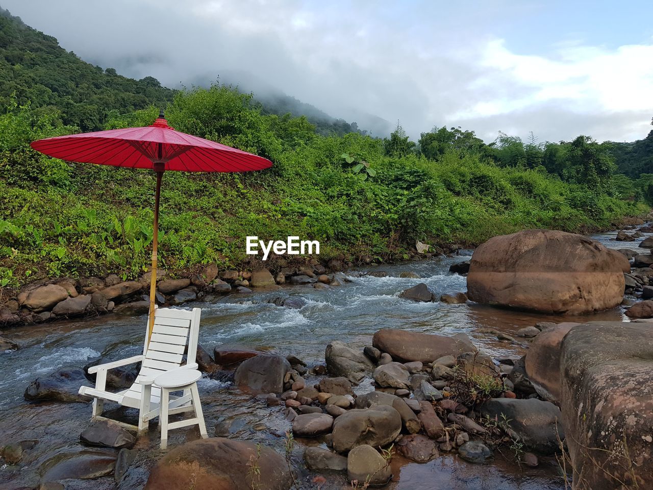 Relaxing area next to the river with trees, rocks against sky