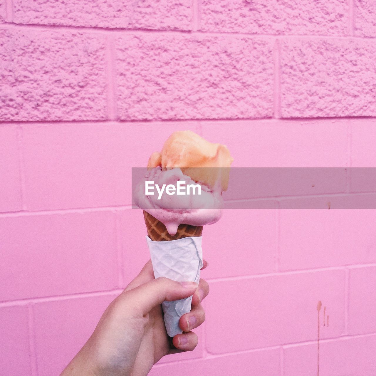 Close-up of hand holding ice cream cone by wall