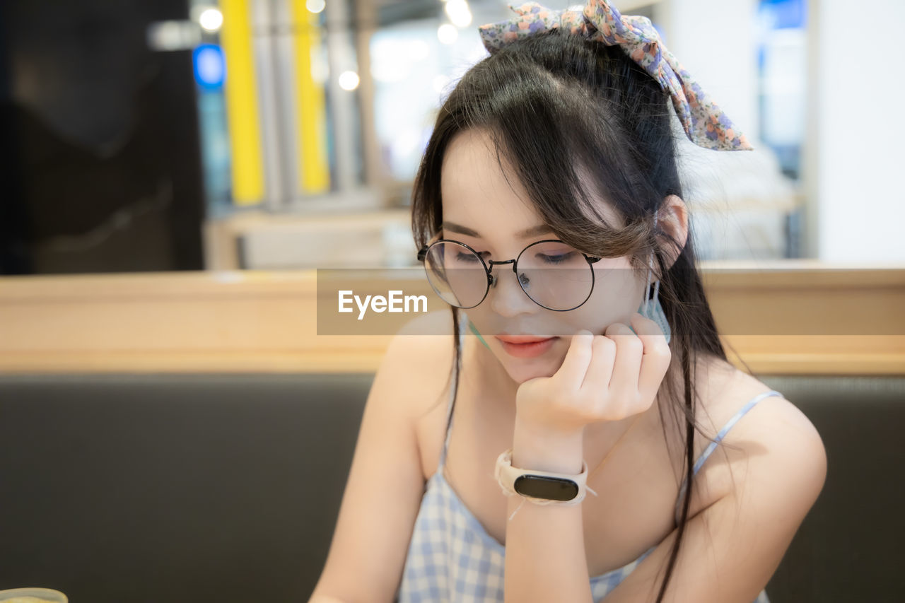Close-up of young woman wearing eyeglasses looking down in restaurant