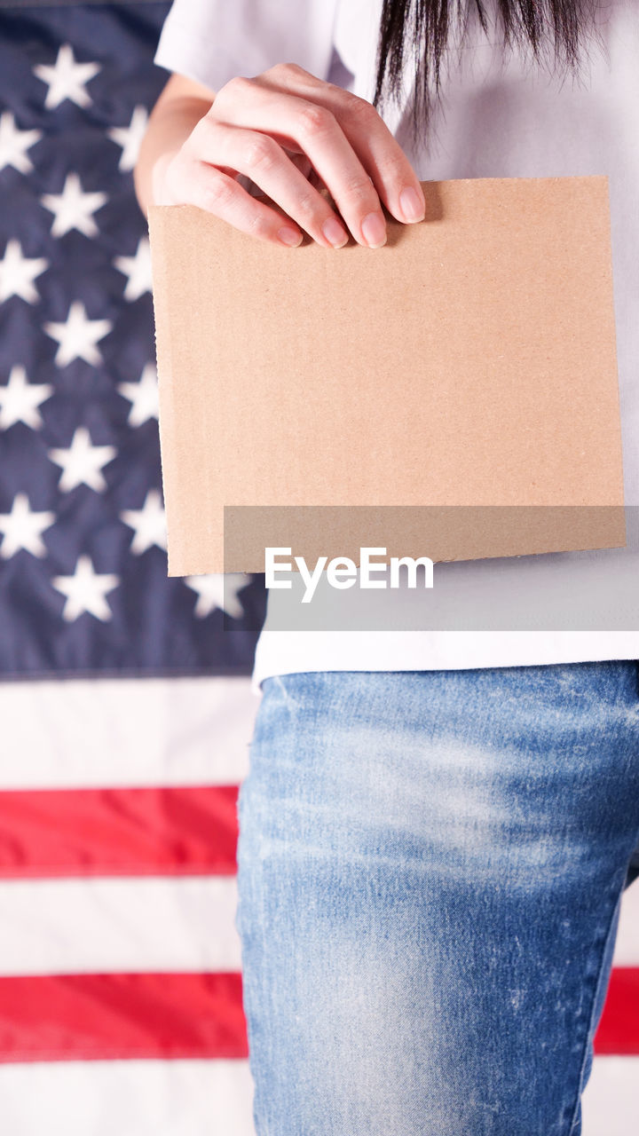 Young woman holds empty cardboard against american flag