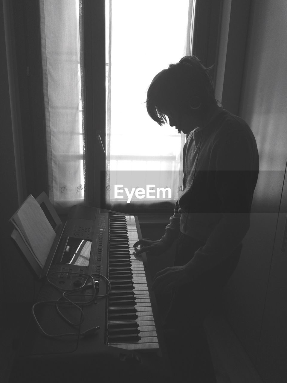 Side view of silhouette boy playing piano while standing at home