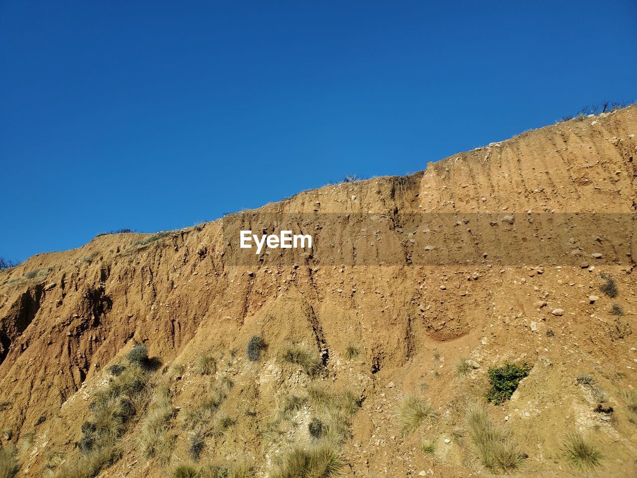 Low angle view of rocky mountain against clear blue sky