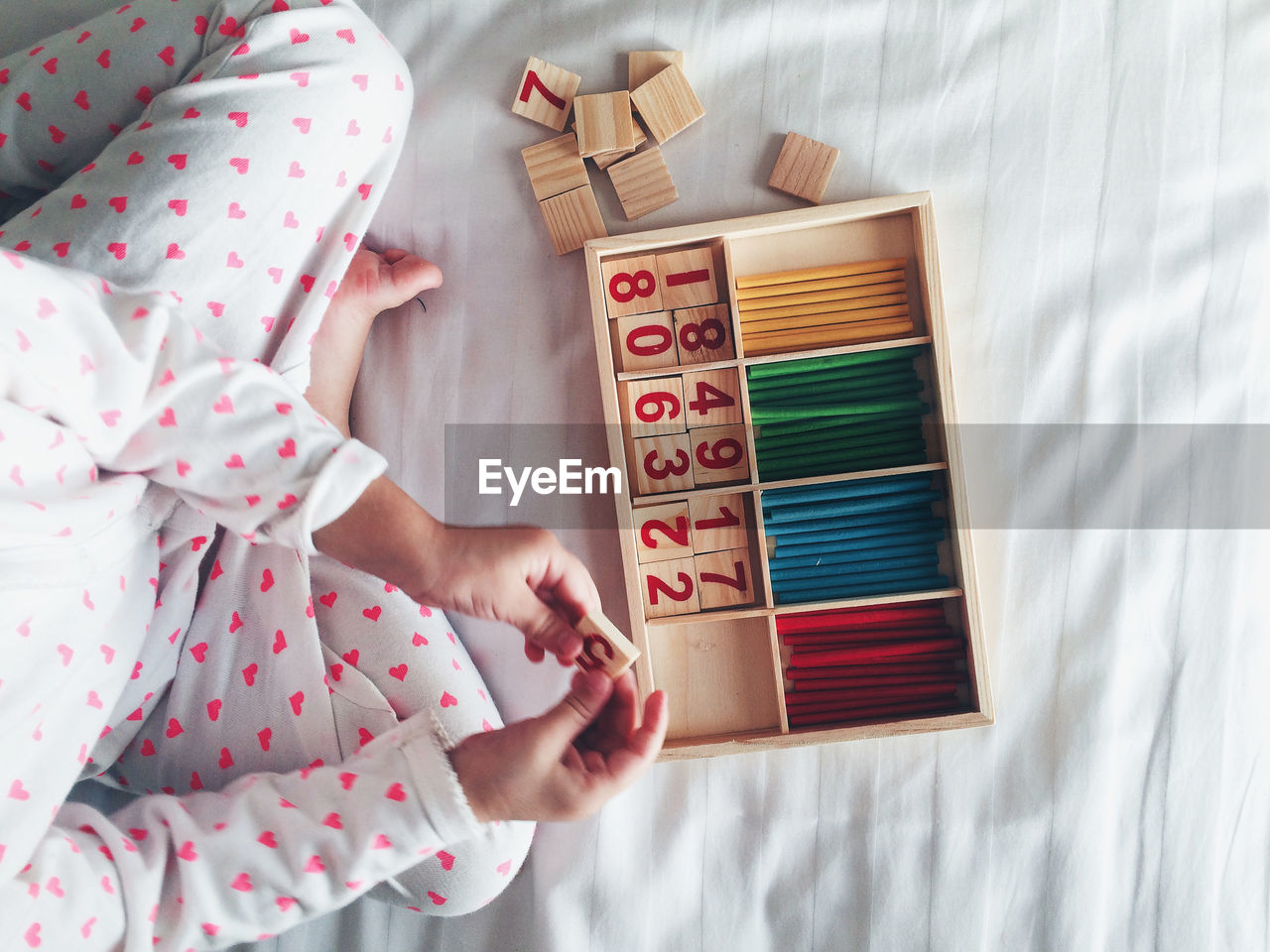 High angle view of child arranging blocks with number in box on bed