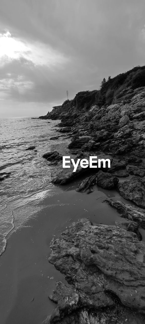 water, sea, land, sky, beach, coast, rock, cloud, ocean, scenics - nature, beauty in nature, wave, nature, shore, black and white, environment, monochrome, monochrome photography, travel destinations, horizon, body of water, tranquility, no people, coastline, landscape, sand, outdoors, travel, tranquil scene, wind wave, tourism, bay, seascape, trip, non-urban scene, holiday, vacation, motion, day, horizon over water, dramatic sky, sports
