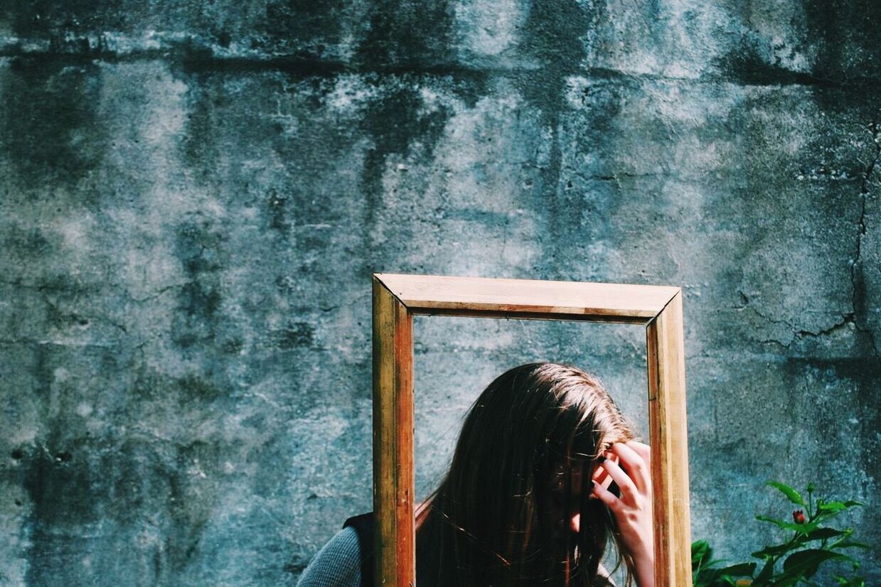 Sad woman by wooden frame against old wall