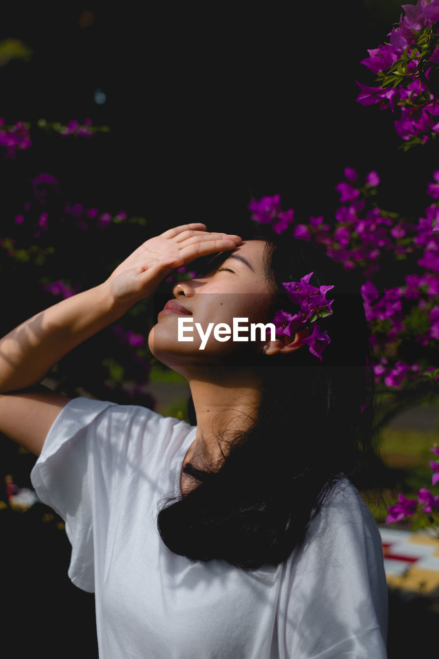 Woman shielding eyes against blooming purple flowers