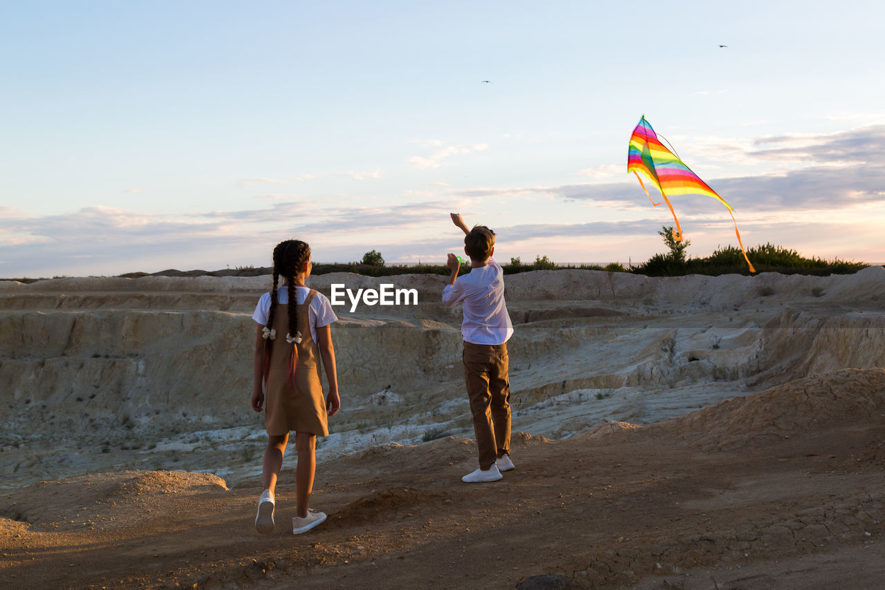 Children with a kite on a high rock near the canyon in the rays at sunset.