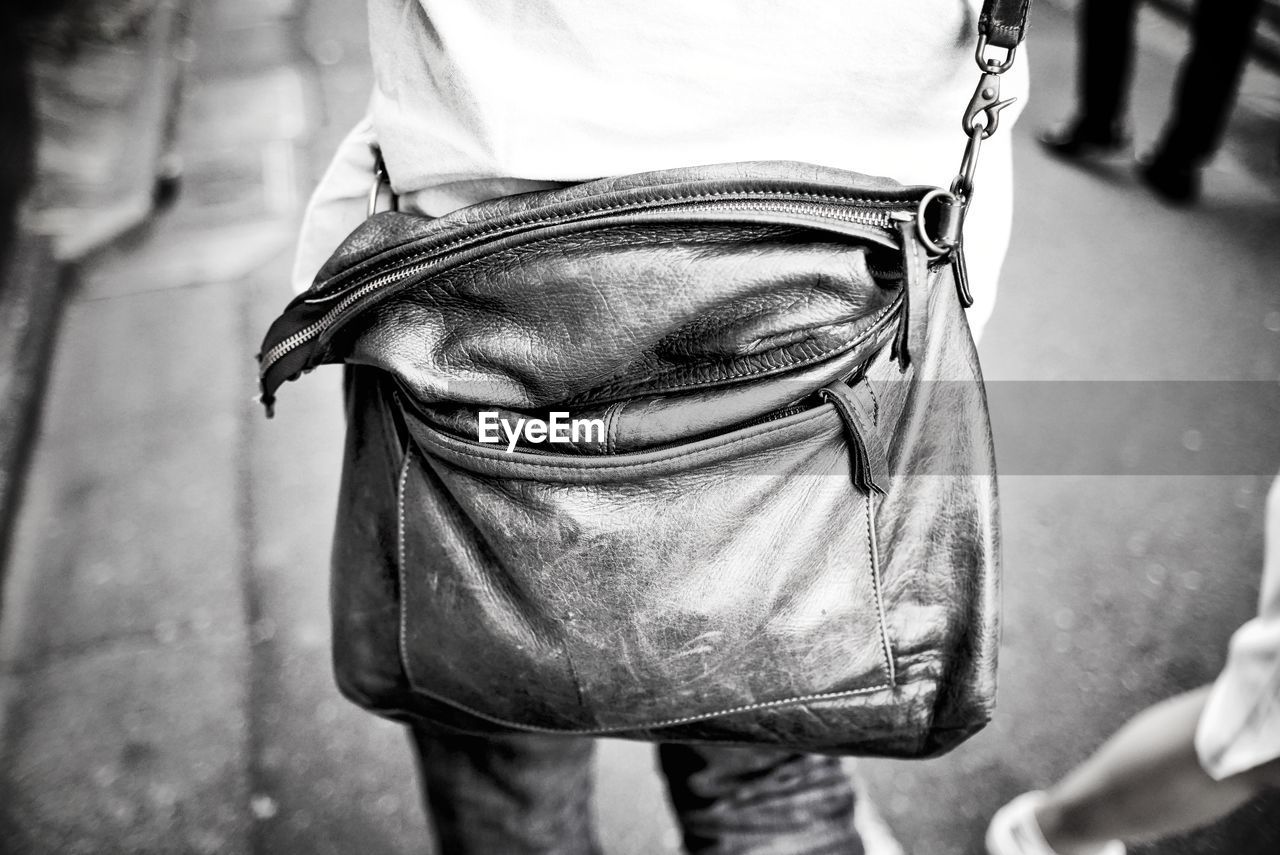 Midsection of man with shoulder bag standing on street