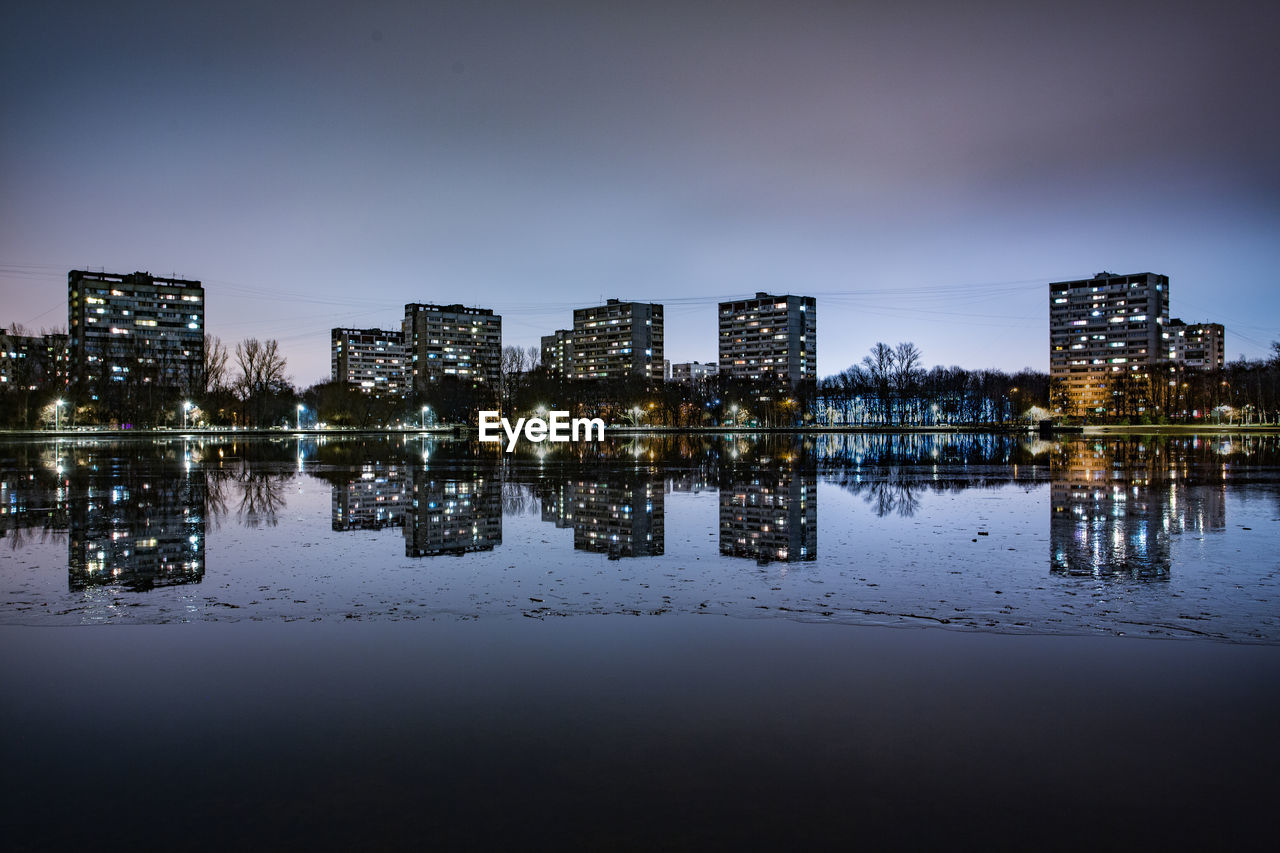 Illuminated buildings by river against sky at night