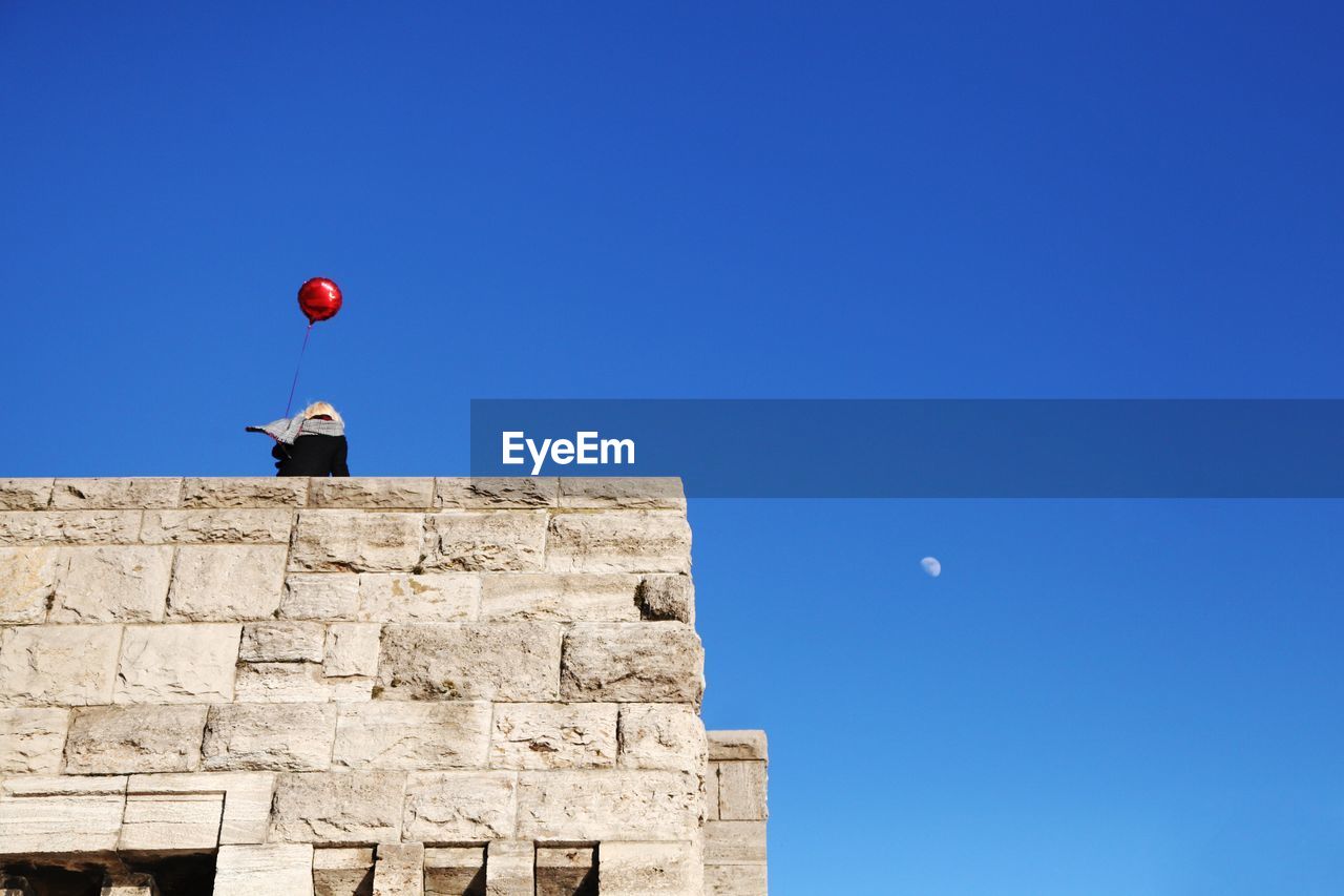 Low angle view of person on a tower holding red balloon against blue sky