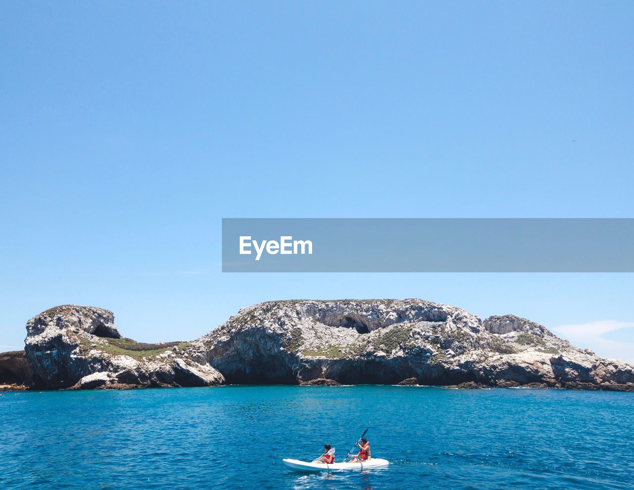 People kayaking in sea against clear blue sky