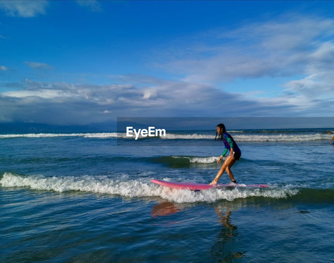 Teenage girl surfing on sea against sky