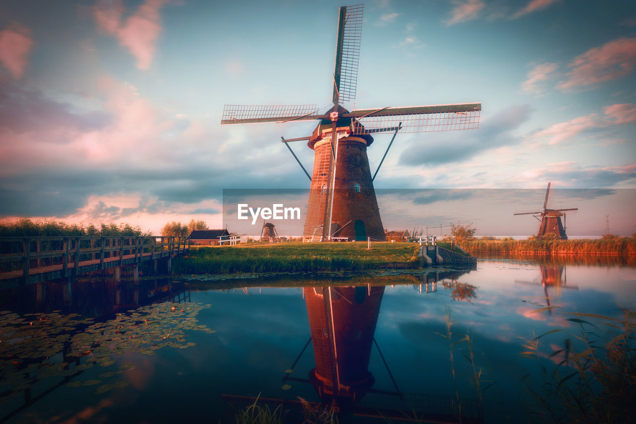 Traditional windmills by lake against cloudy sky