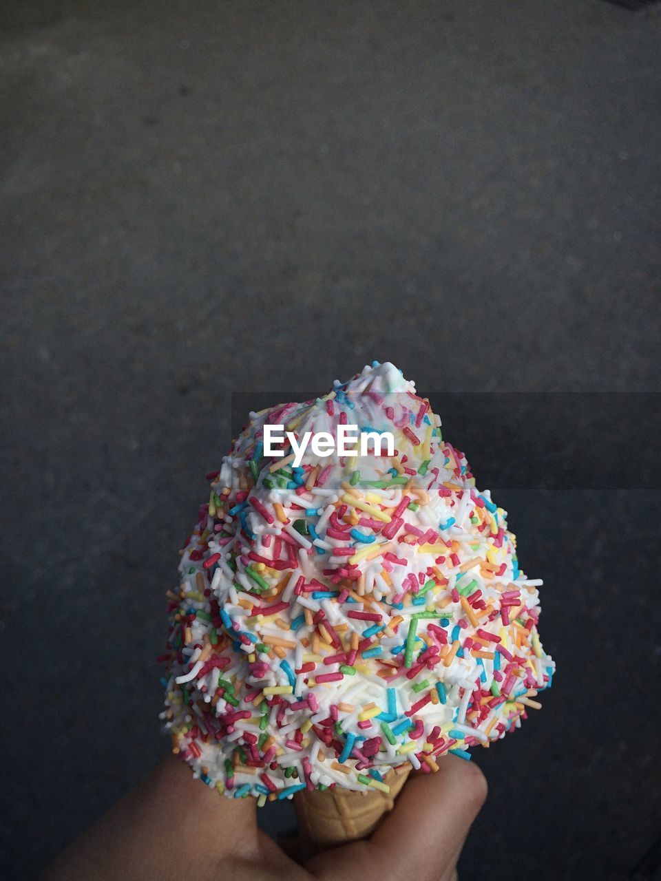 Close-up of hand holding ice cream cone against black background