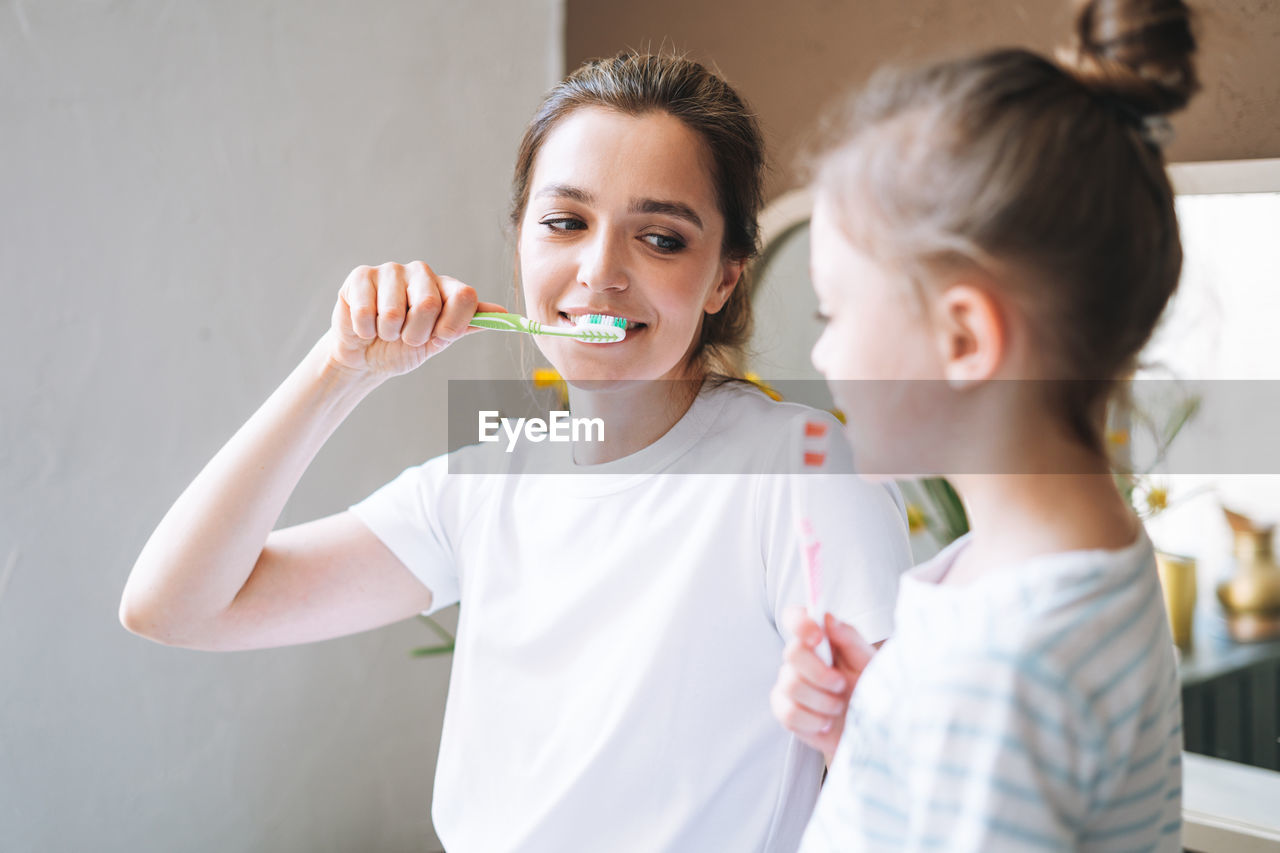 Young mother woman with little tween girl daughter in pajamas brushing their teeth at home