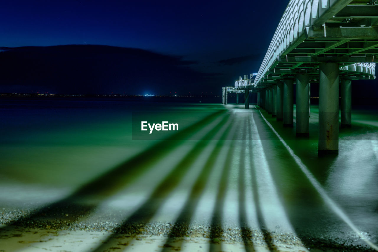 Light trails of an illuminated pier on the water at night 