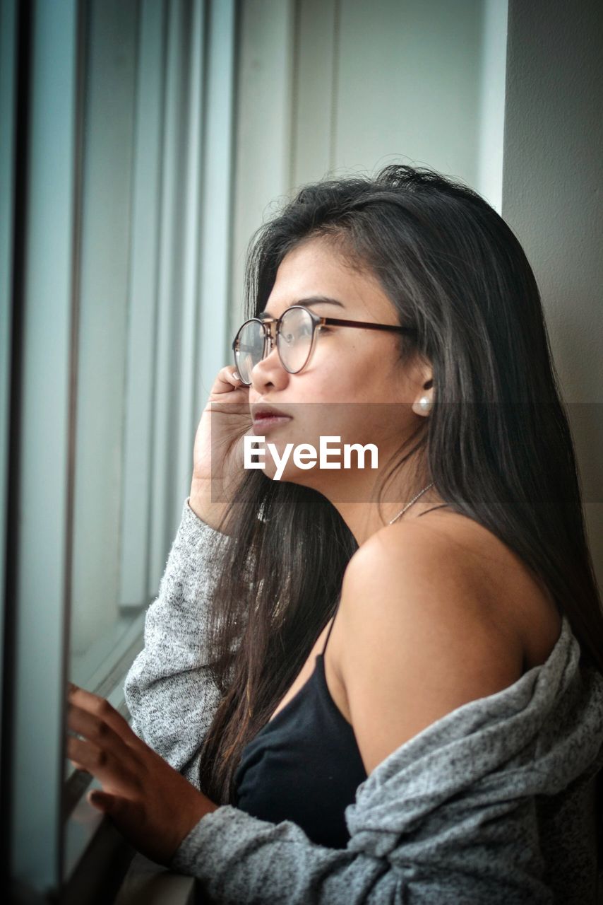 Side view of woman standing by window at home